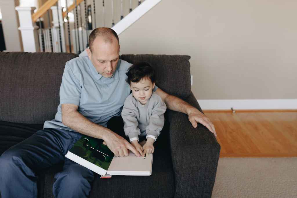 father and child sitting on gray sofa with a book